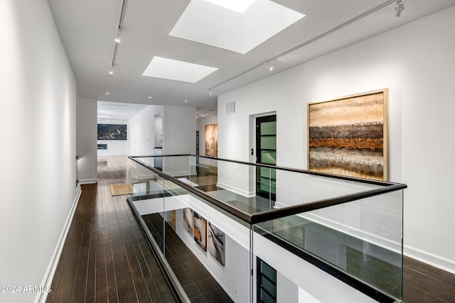 hallway featuring track lighting, a skylight, baseboards, and dark wood-style floors