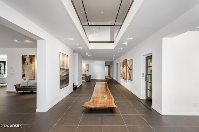 hallway featuring a skylight, a tray ceiling, and dark tile patterned flooring