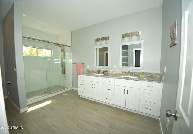 bathroom featuring wood tiled floor, a sink, a shower stall, and double vanity