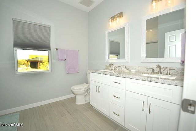 full bathroom featuring toilet, double vanity, baseboards, and a sink