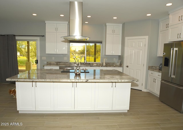 kitchen featuring white cabinetry, a healthy amount of sunlight, stainless steel fridge with ice dispenser, an island with sink, and island exhaust hood