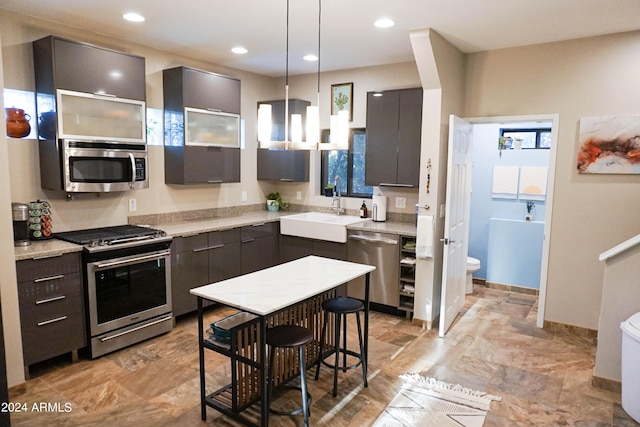 kitchen featuring sink, hanging light fixtures, light stone counters, a kitchen bar, and appliances with stainless steel finishes