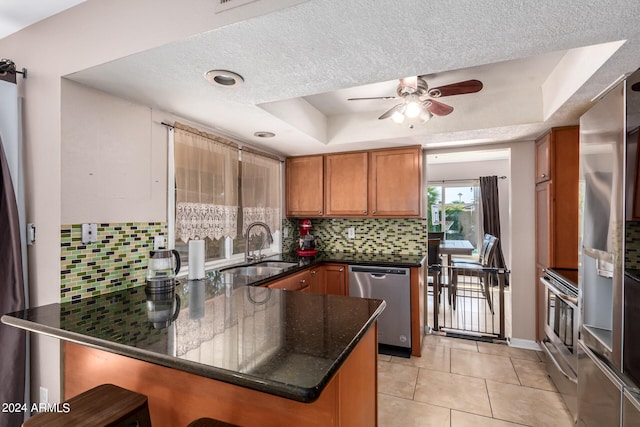 kitchen featuring stainless steel appliances, tasteful backsplash, sink, kitchen peninsula, and a tray ceiling