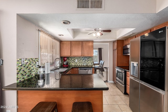 kitchen featuring kitchen peninsula, decorative backsplash, stainless steel appliances, and a raised ceiling