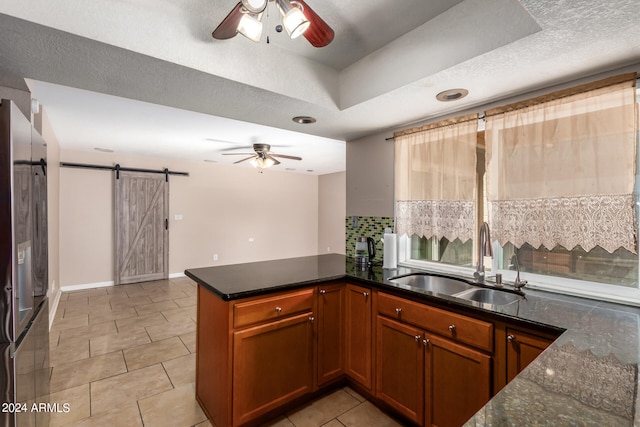 kitchen with stainless steel fridge, sink, kitchen peninsula, a barn door, and a textured ceiling