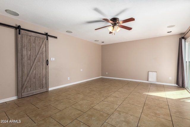 spare room featuring ceiling fan, light tile patterned flooring, and a barn door