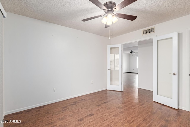 unfurnished bedroom with ceiling fan, dark hardwood / wood-style floors, a textured ceiling, and french doors