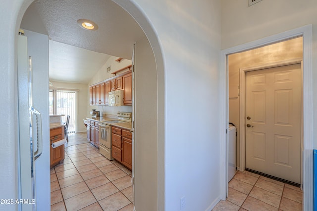 kitchen featuring lofted ceiling, white appliances, a textured ceiling, light tile patterned flooring, and washer / clothes dryer