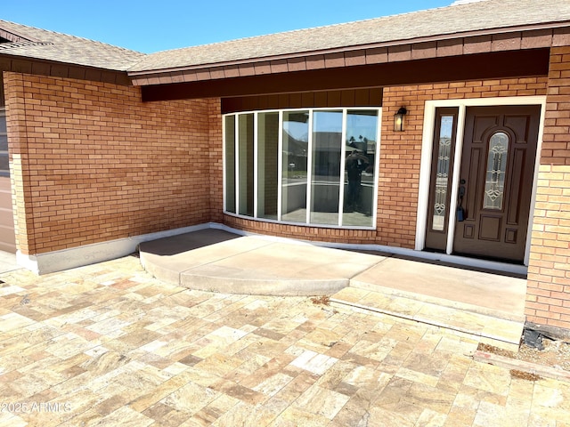 doorway to property with a patio, brick siding, and a shingled roof