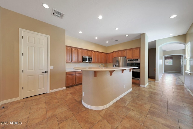 kitchen with stainless steel appliances, a breakfast bar, visible vents, light countertops, and an island with sink