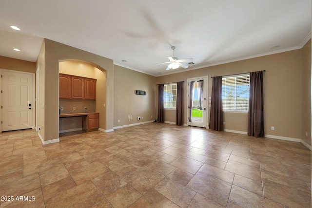 unfurnished living room with crown molding, baseboards, a ceiling fan, and built in study area