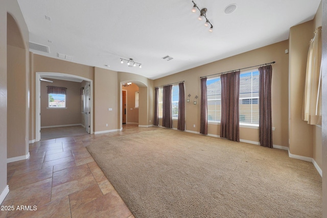 unfurnished living room featuring arched walkways, light colored carpet, visible vents, and a healthy amount of sunlight