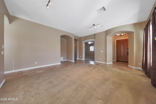 unfurnished living room with light carpet, visible vents, arched walkways, an inviting chandelier, and track lighting