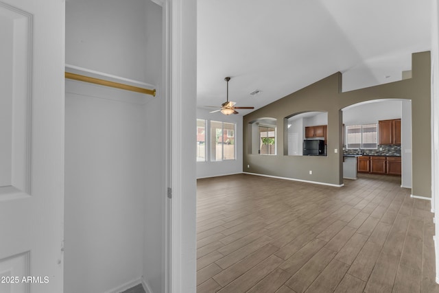 unfurnished living room with lofted ceiling, baseboards, ceiling fan, wood finished floors, and arched walkways