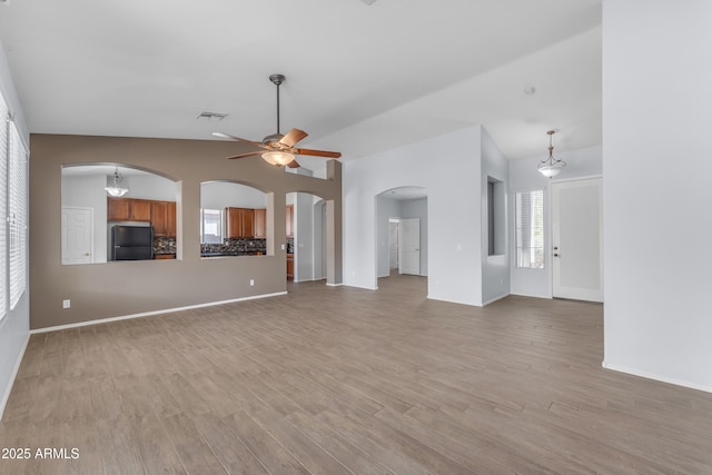 unfurnished living room featuring a ceiling fan, baseboards, visible vents, arched walkways, and light wood-type flooring
