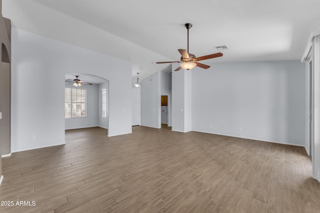 unfurnished living room with visible vents, wood finished floors, ceiling fan, and arched walkways
