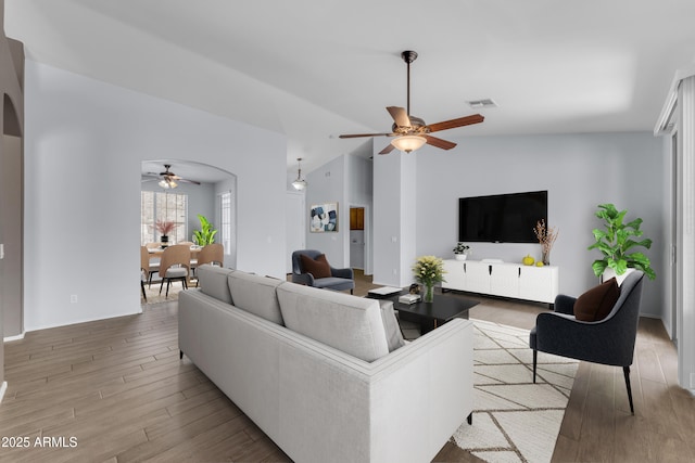 living room featuring wood finished floors, a ceiling fan, visible vents, baseboards, and arched walkways