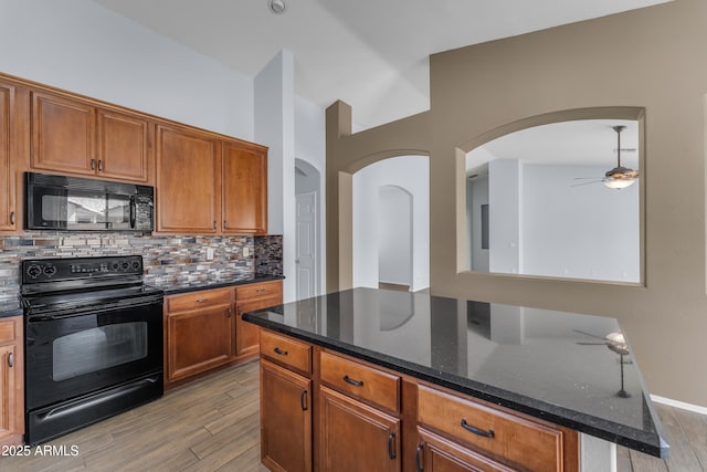 kitchen with tasteful backsplash, dark stone countertops, black appliances, light wood finished floors, and a ceiling fan