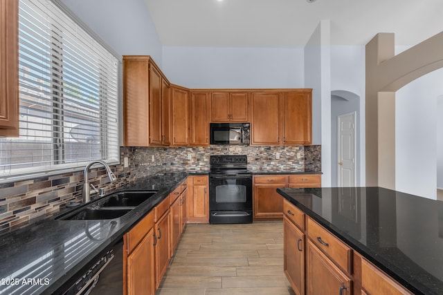 kitchen featuring light wood finished floors, a sink, dark stone countertops, black appliances, and tasteful backsplash