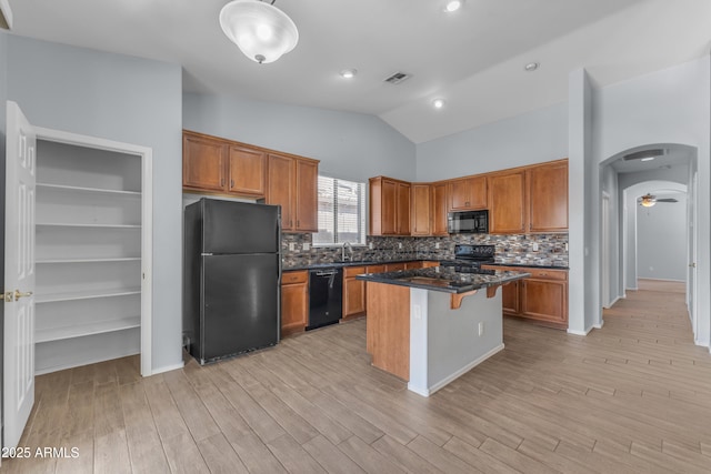 kitchen featuring lofted ceiling, visible vents, a kitchen island, black appliances, and tasteful backsplash