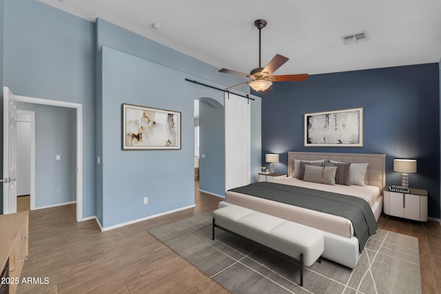 bedroom with wood finished floors, visible vents, baseboards, ceiling fan, and arched walkways