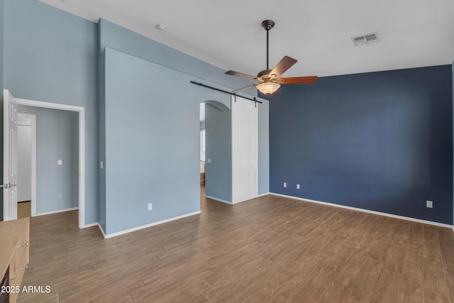 unfurnished room with a ceiling fan, wood finished floors, visible vents, and arched walkways