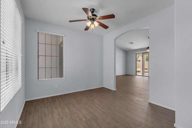 unfurnished room with a ceiling fan, baseboards, wood finished floors, and arched walkways