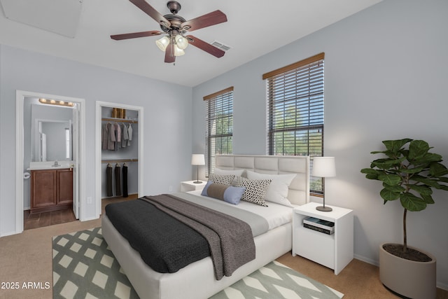 bedroom with a closet, baseboards, ensuite bath, visible vents, and light colored carpet