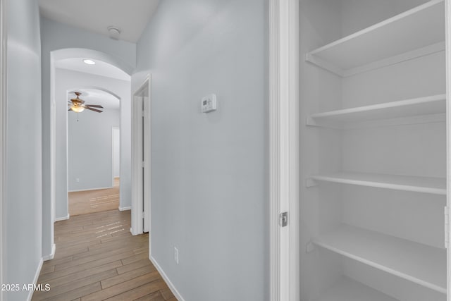 hall featuring arched walkways, baseboards, and wood finished floors