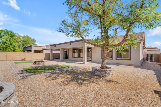 rear view of property featuring a tile roof, a patio, stucco siding, a fenced backyard, and an outdoor fire pit