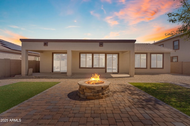 back of property at dusk with a patio, a fire pit, stucco siding, and a fenced backyard
