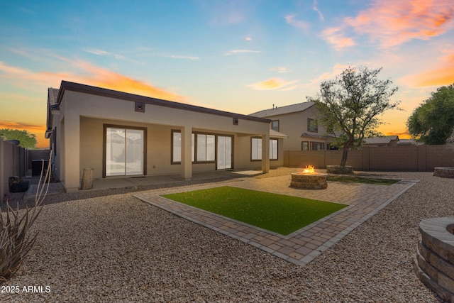 rear view of property featuring a patio area, stucco siding, a fire pit, and a fenced backyard