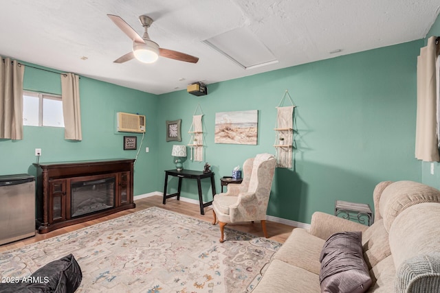 living area featuring a ceiling fan, a wall mounted AC, wood finished floors, baseboards, and attic access