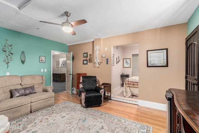 living area with baseboards, wood finished floors, and ceiling fan