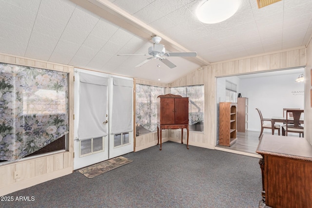 interior space with wood walls, vaulted ceiling with beams, a ceiling fan, and carpet floors