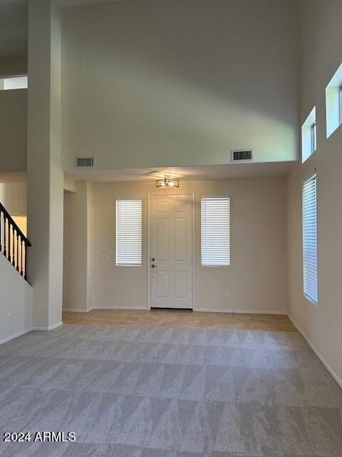 interior space with visible vents, light colored carpet, stairs, and a high ceiling