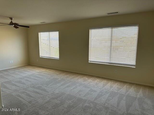 carpeted empty room with a ceiling fan, visible vents, and baseboards