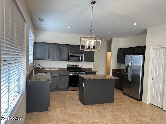 kitchen with a sink, appliances with stainless steel finishes, dark stone countertops, and a center island