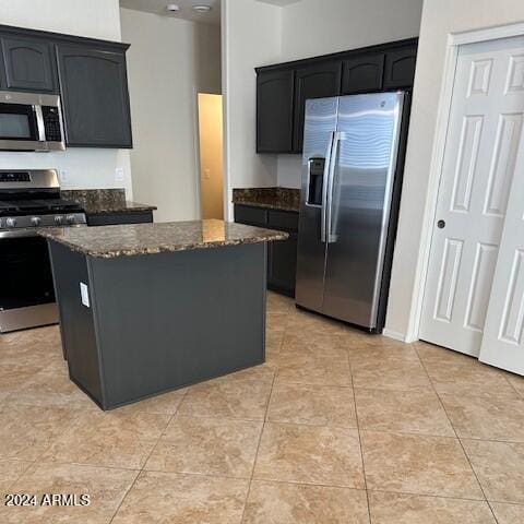 kitchen featuring dark stone countertops, light tile patterned flooring, appliances with stainless steel finishes, dark cabinets, and a center island