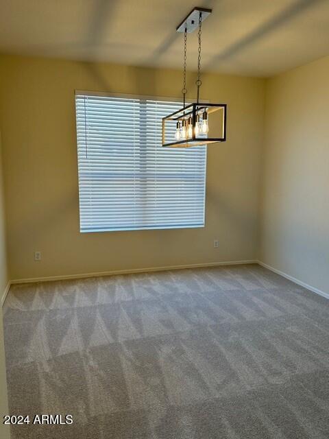 carpeted spare room with baseboards and a chandelier