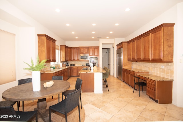 kitchen with a breakfast bar area, built in appliances, light stone countertops, and a center island