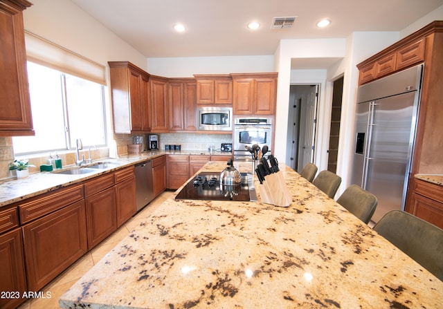 kitchen featuring light stone counters, sink, tasteful backsplash, built in appliances, and a breakfast bar