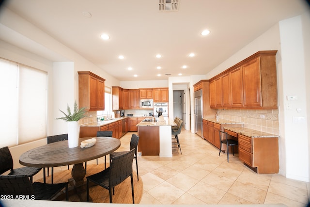 kitchen featuring light stone counters, backsplash, built in appliances, a center island, and a breakfast bar area