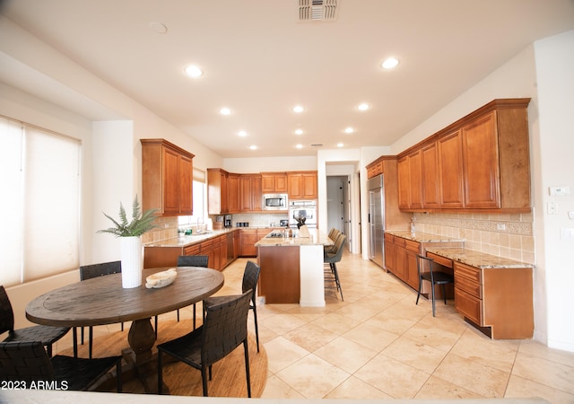 kitchen featuring tasteful backsplash, a kitchen island, stainless steel microwave, light stone counters, and a kitchen bar