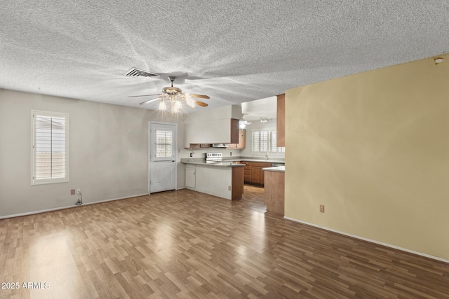 unfurnished living room with a textured ceiling, wood finished floors, visible vents, baseboards, and a ceiling fan