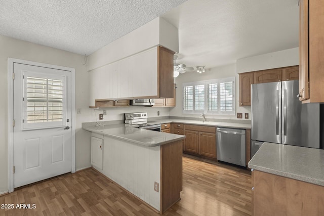 kitchen featuring light wood-style flooring, a peninsula, a sink, light countertops, and appliances with stainless steel finishes