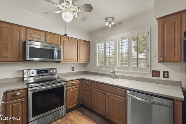 kitchen with light countertops, appliances with stainless steel finishes, a ceiling fan, a sink, and light wood-type flooring