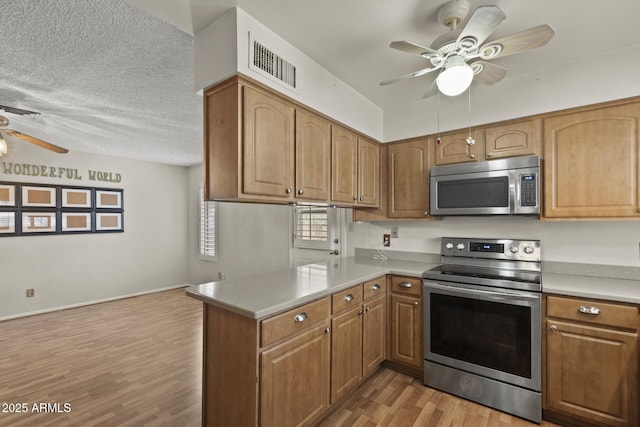 kitchen with ceiling fan, a peninsula, visible vents, appliances with stainless steel finishes, and light wood finished floors