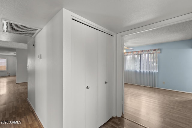 hallway featuring visible vents, a textured ceiling, baseboards, and wood finished floors