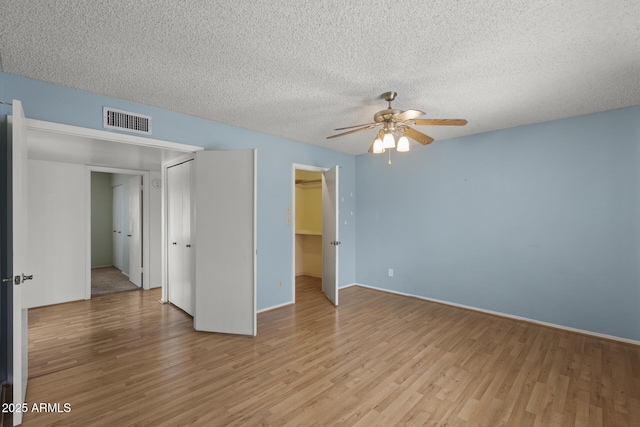 unfurnished bedroom featuring a closet, visible vents, light wood-style floors, ceiling fan, and a textured ceiling